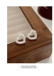 Detail of S925 sterling silver hollow heart stud earrings on a vintage wooden jewelry box