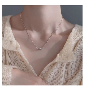 Close-up of minimalist S925 silver bow pendant necklace worn on elegant neckline
