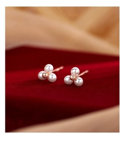 Détail de boucles d'oreilles à trois perles dorées roses sur fond de velours rouge