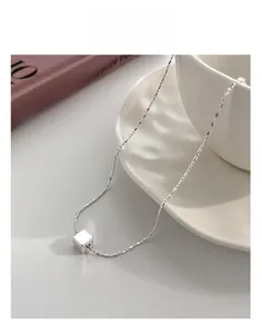 Macro detail of polished silver cube pendant on a cylindrical link chain necklace
