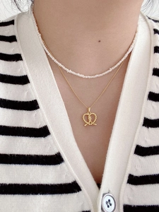 Close-up of layered S925 silver necklace with pearls and golden twist heart knot pendant