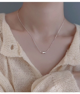Detail of silver bow pendant on a fine snake chain necklace worn with a knit sweater
