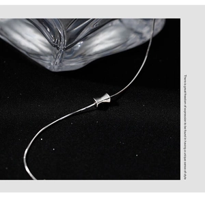 Detailed view of silver bow hourglass pendant necklace on elegant black background