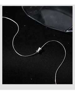 Macro shot of silver bow pendant on sleek snake chain over textured black background