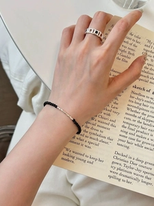 Detail of silver hollow geometric ring and black beaded bracelet on model reading a book