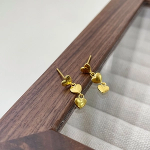 Détail macro de trois boucles d'oreilles cœurs dorés sur un écrin à bijoux en bois