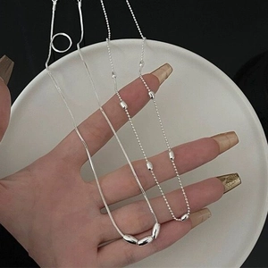 Detail of two layered S925 sterling silver necklaces with oval beads on white ceramic tray