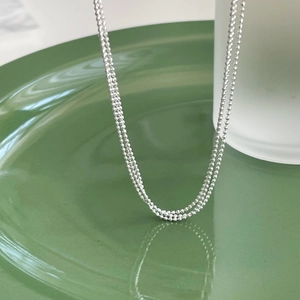 Detailed view of shimmering silver double-layered bead chain over a green plate