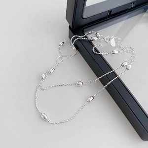 Detail of silver bead chain necklace showing polished oval grains on black display