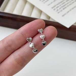 Gros plan de boucles d'oreilles argentées à trois cœurs tenues sur plateau bois