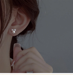 Macro detail of S925 silver bow earring featuring a polished white pearl on model ear