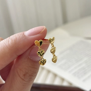 Vue macro de boucles d'oreilles pendantes triple cœur doré en argent S925 poli