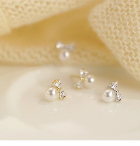 Macro shot of silver bow pearl stud earrings with sparkling rhinestones and warm pearl finish