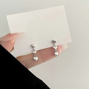 Vue détaillée des boucles d'oreilles triple cœur en argent sur carte bijou