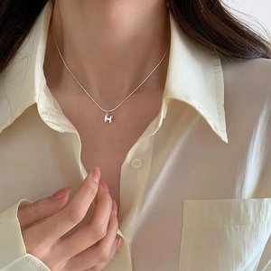 Collier avec pendentif H stéréoscopique en argent S925 porté sur une chemise blanche