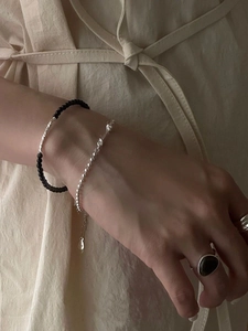 Layered S925 silver beaded bracelets and black onyx rings worn by a model in soft light