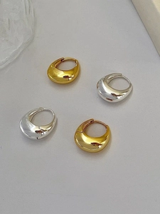 Macro detail of polished gold and silver water drop hoop earrings on a grey background