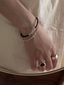 Detail view of S925 silver beaded bracelets and black onyx ring on a linen background