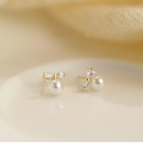 Macro shot of bow-shaped zircon and white pearl stud earring on a beige tray