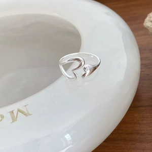 Detail view of silver S925 liquid metal style open ring on white ceramic and wood surface