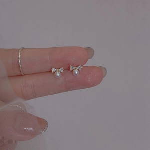 Detailed view of silver bow-shaped pearl earring with rhinestones held in hand