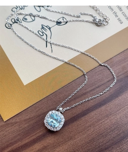 Detail shot of a square blue zircon pendant with silver chain on an artistic card