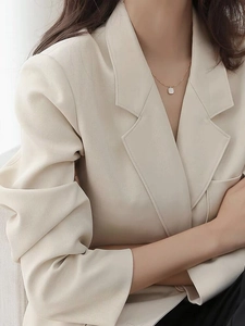 Detail of a square white shell pendant on a fine S925 silver chain worn with a beige blazer