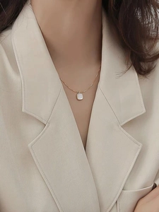 Close-up of a square white mother-of-pearl pendant necklace worn by a model in a suit