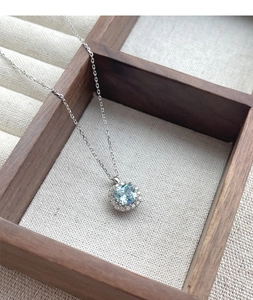 Detail of S925 silver necklace with blue cushion cut zircon pendant on a wood tray