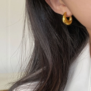Close-up of a person wearing gold teardrop hoop earrings with high-polish mirror finish