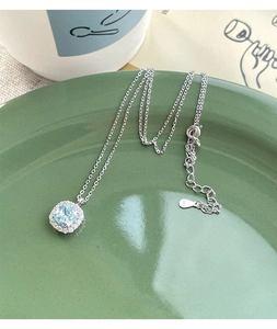 Detail of S925 silver necklace featuring a square blue zircon pendant on a green ceramic plate