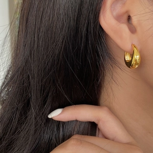 Close-up of elegant gold teardrop earrings worn by a model with polished mirror finish