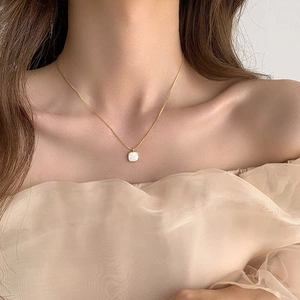 Close-up of elegant square white shell pendant on 18K gold chain worn by a model