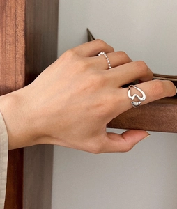 Detailed view of hollow heart silver ring and beaded band worn on a hand in natural light