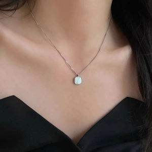 Detail shot of a square white shell pendant on a fine silver box chain worn by a model