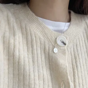 Primo piano di una collana con ciondolo a rosa d'argento su un cardigan color crema