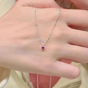 Détail d'un collier en argent S925 avec un petit pendentif cœur rouge porté par une femme