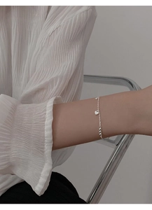 Detail of S925 sterling silver heart charm bracelet worn with white pleated blouse