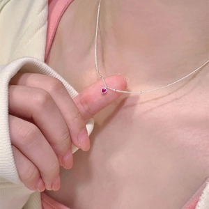 Gros plan d'un collier en argent S925 avec un petit pendentif coeur rouge sur un mannequin