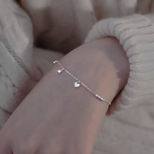 Detail of S925 silver bracelet with sparkling heart charm on woman's wrist