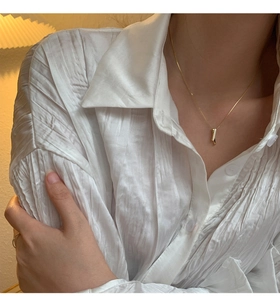 Close-up of gold vertical bar pendant necklace with shimmering detail on white shirt