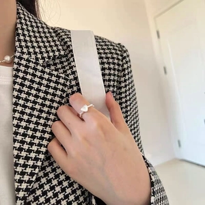 Detail of twisted S925 silver ring with heart motif worn on finger over houndstooth fabric