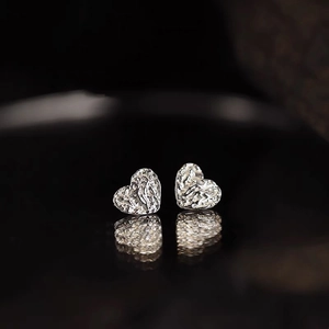 Macro shot of S925 sterling silver heart studs with textured tinfoil surface and reflection