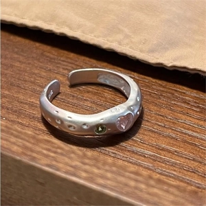 Detail of S925 silver irregular heart ring with pink and green stones on wooden surface