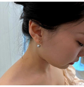 Detail of grey pearl drop earring with fine gold chain worn by a model in warm light