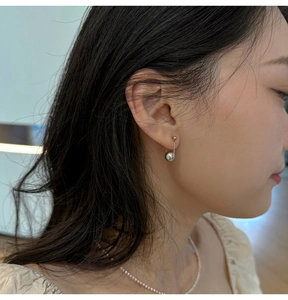 Detail of minimalist S925 silver pearl drop earrings worn by a model in soft indoor light