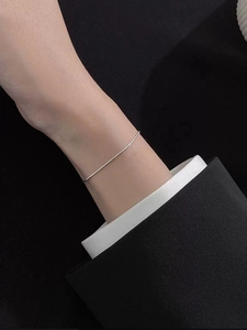Detailed view of a minimalist S925 sterling silver snake chain on a wrist with dark contrast