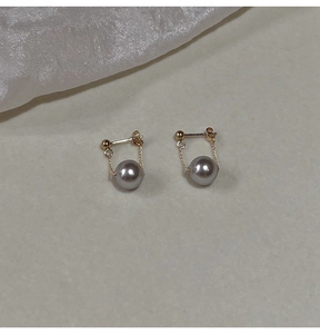 Detailed close-up of dark grey round pearl earrings with golden chain on soft fabric