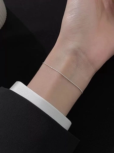 Macro shot of slender S925 silver snake chain bracelet worn on wrist with elegant outfit