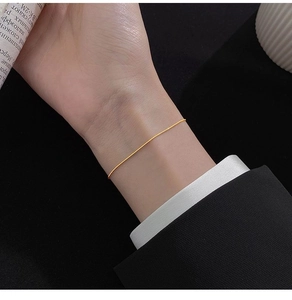 Close-up of minimalist gold snake chain bracelet on a wrist with black blazer sleeve